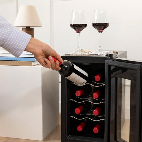 Persona che preleva bottiglia di vino da cantinetta da 8 bottiglie 25 litri in ambiente domestico elegante con calici